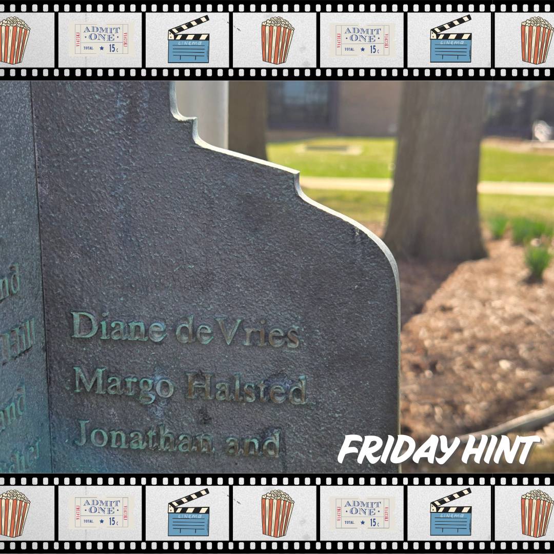 Piece of metal with names etched into it with greenery and a building in the background